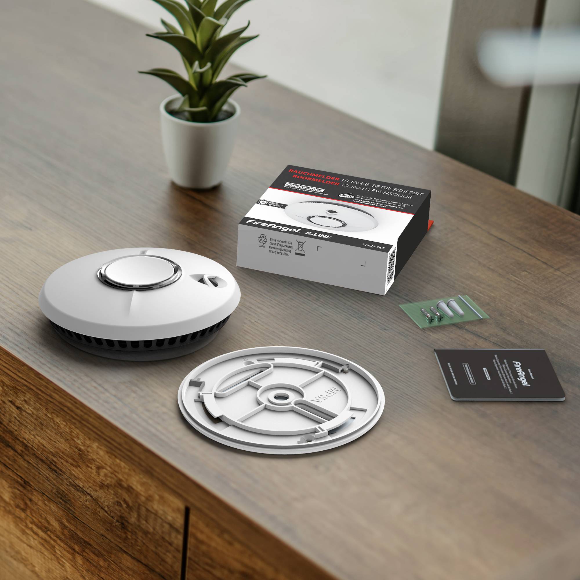 Ein Rauchmelder-Set auf einem Holztisch, bestehend aus dem Detektor, der Befestigungsplatte, ungeöffneter Verpackung, Schrauben und einer Bedienungsanleitung.