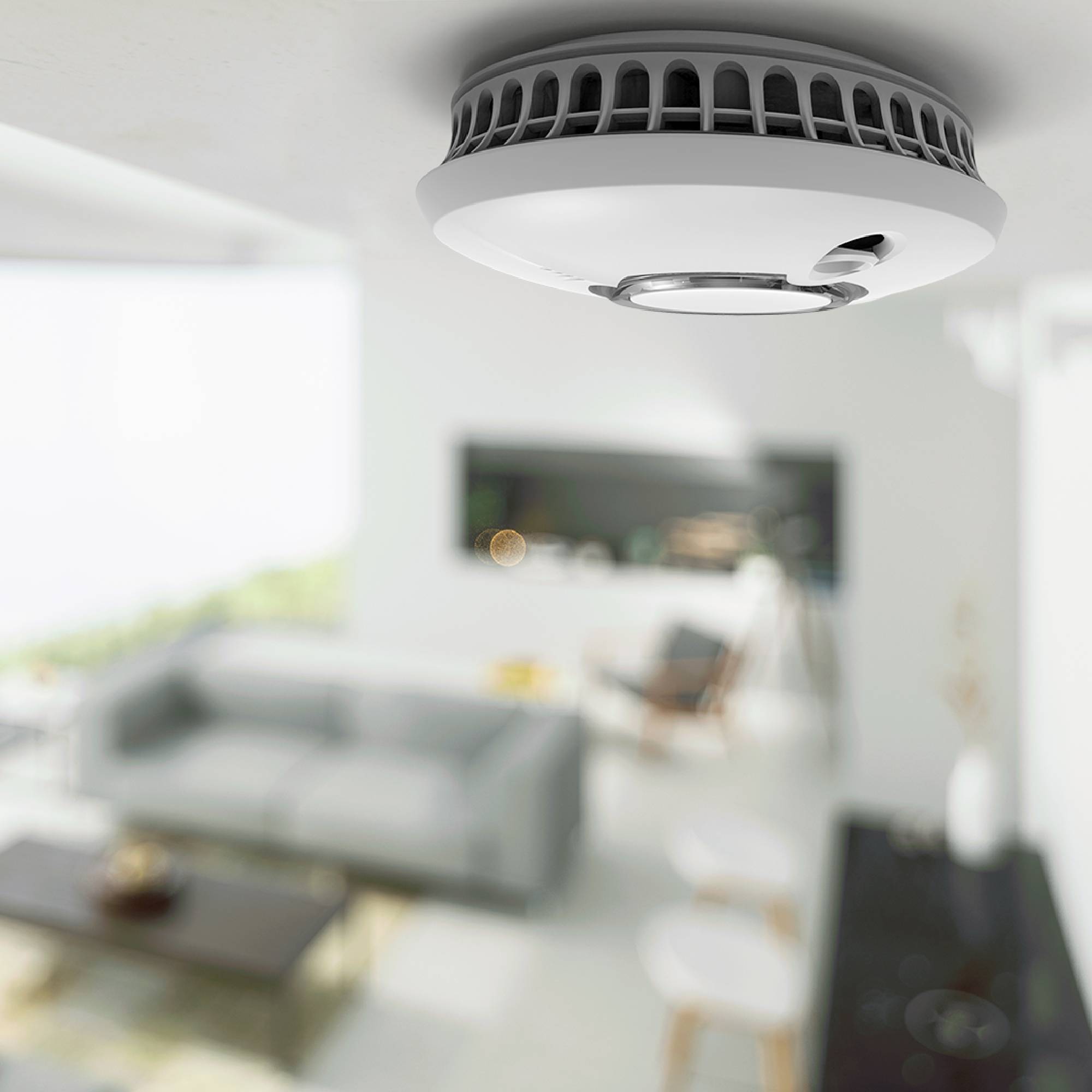 Ein Rauchmelder ist an der Decke eines modernen Wohnzimmers montiert. Im Hintergrund sind ein Sofa und ein Tisch zu sehen.