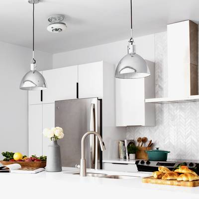 Helle, moderne Küche mit weißen Schränken, Metallleuchten, Obst auf dem Tisch und einem Edelstahlkühlschrank.
