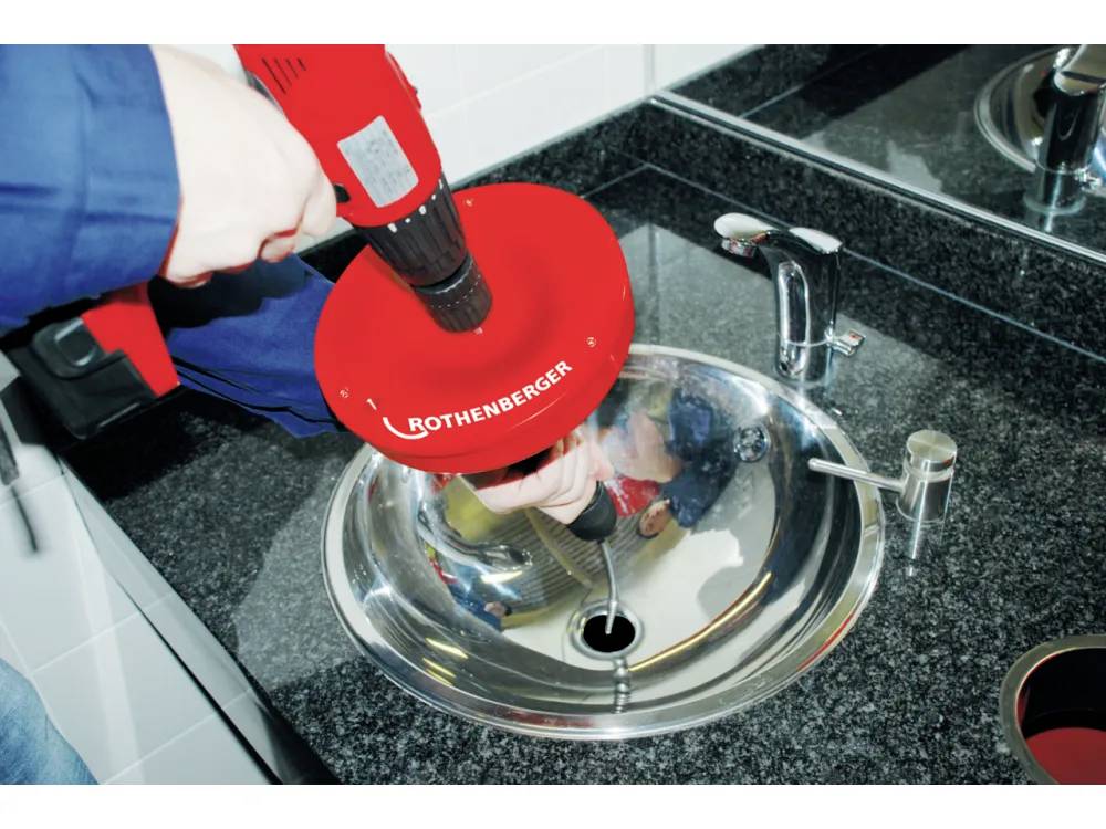 Eine Person, die ein rotes Rothenberger-Klempnerwerkzeug verwendet, um ein Badezimmerwaschbecken zu entklotzen.