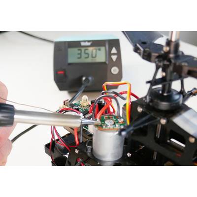 Eine Person lötet an einer Platine mit einem Lötkolben. Im Hintergrund zeigt ein digitales Thermometer 350 Grad Celsius an.