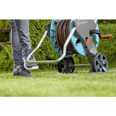 Person tritt auf den Fußhebel eines Schlauchwagens auf einer Rasenfläche. Der Wagen hat einen aufgewickelten Gartenschlauch.