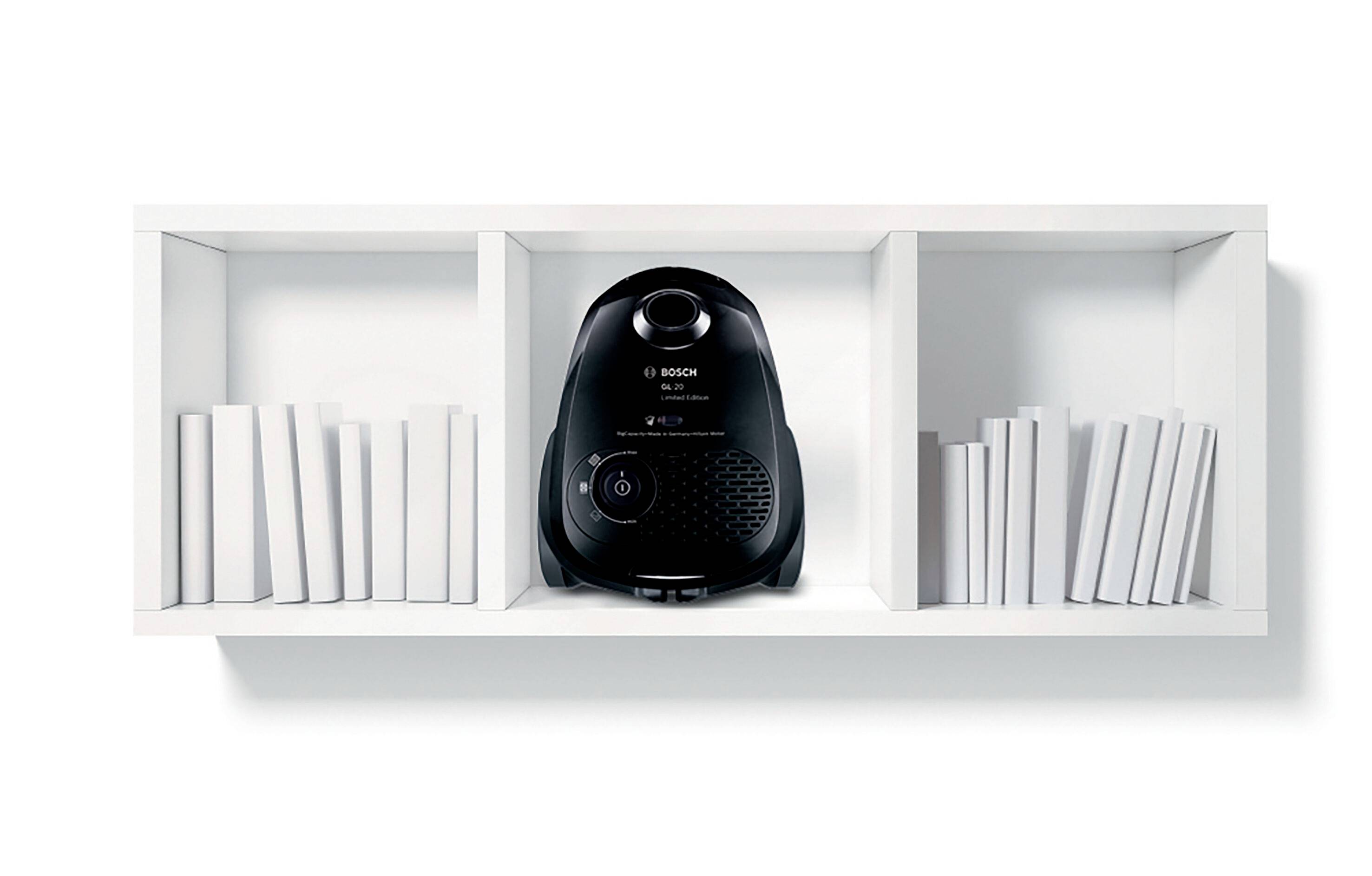 Ein schwarzer Staubsauger im Regal, umgeben von weißen Büchern, kontrastiert minimalistisch auf weißem Hintergrund.