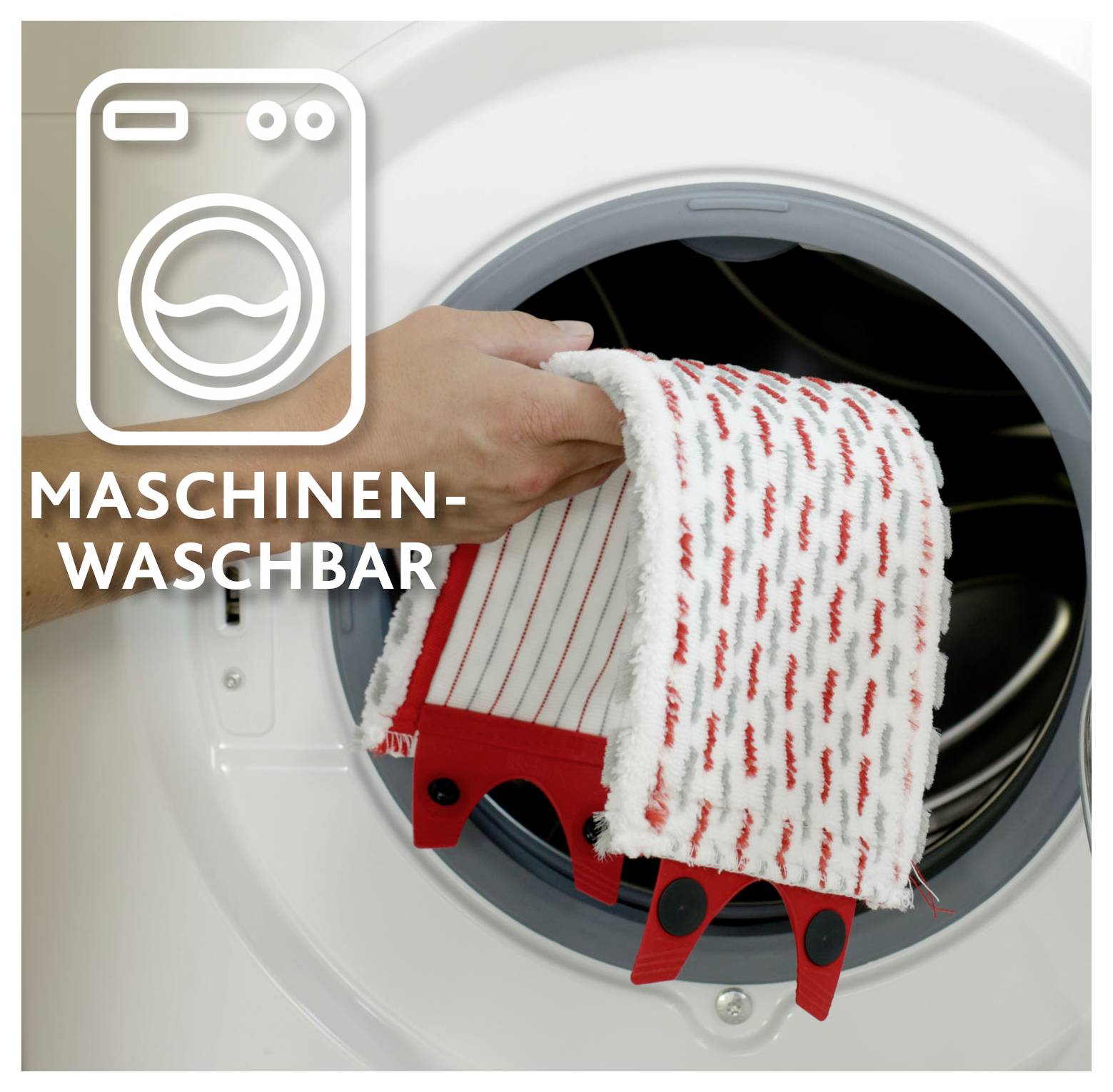 Hand beim Einlegen eines rot-weißen Textilartikels in eine Waschmaschine, mit der Aufschrift "MASCHINEN-WASCHBAR" zur Anzeige von Maschinenwäsche geeignet.