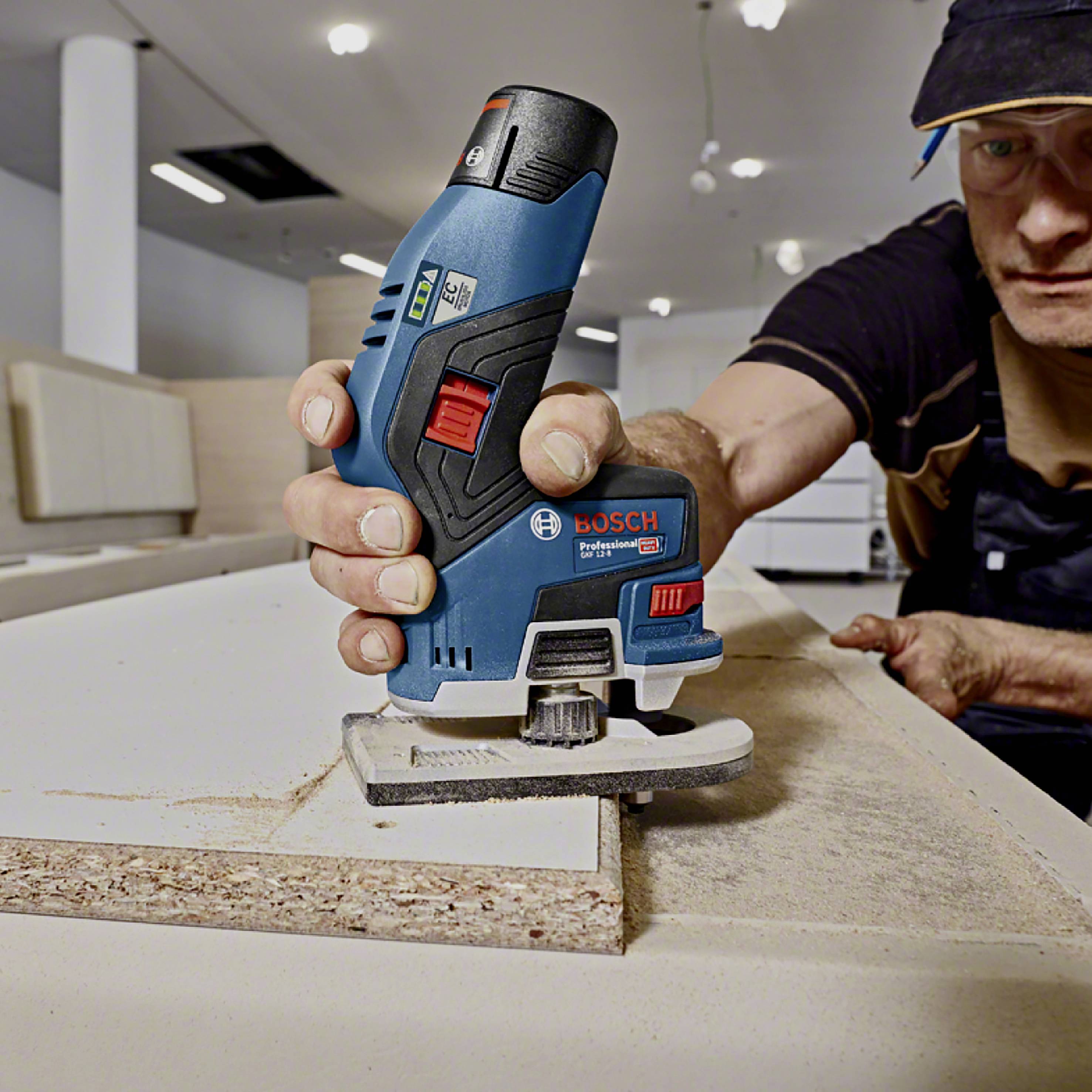 Eine Person benutzt eine blaue Bosch Elektro-Stichsäge, um eine Holzplatte zu schneiden. Die Umgebung scheint eine Werkstatt zu sein.