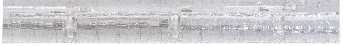 Glasartige Struktur mit parallel verlaufenden Rillen und vertikalen Markierungen.