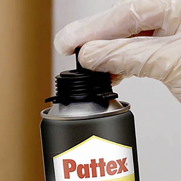 Eine Hand mit Handschuh hält eine schwarze Flasche mit der Aufschrift "Pattex" und ist im Begriff, Klebstoff aufzutragen.