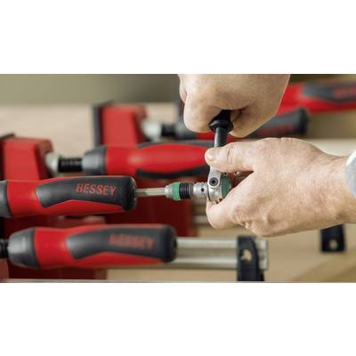 Eine Person spannt eine Schraubzwinge an einem Holzprojekt an. Im Hintergrund sind weitere rote Schraubzwingen sichtbar.