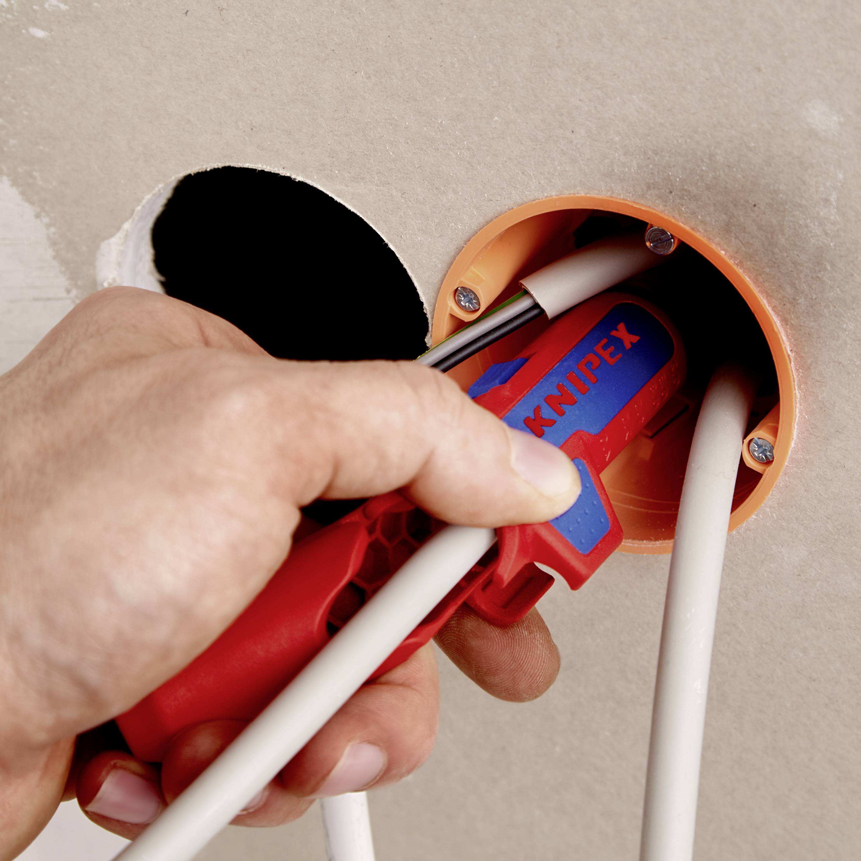 Eine Hand, die ein rotes Werkzeug verwendet, um Kabel in einer runden Wanddose zu installieren. Reparatur- oder Installationsprozess.