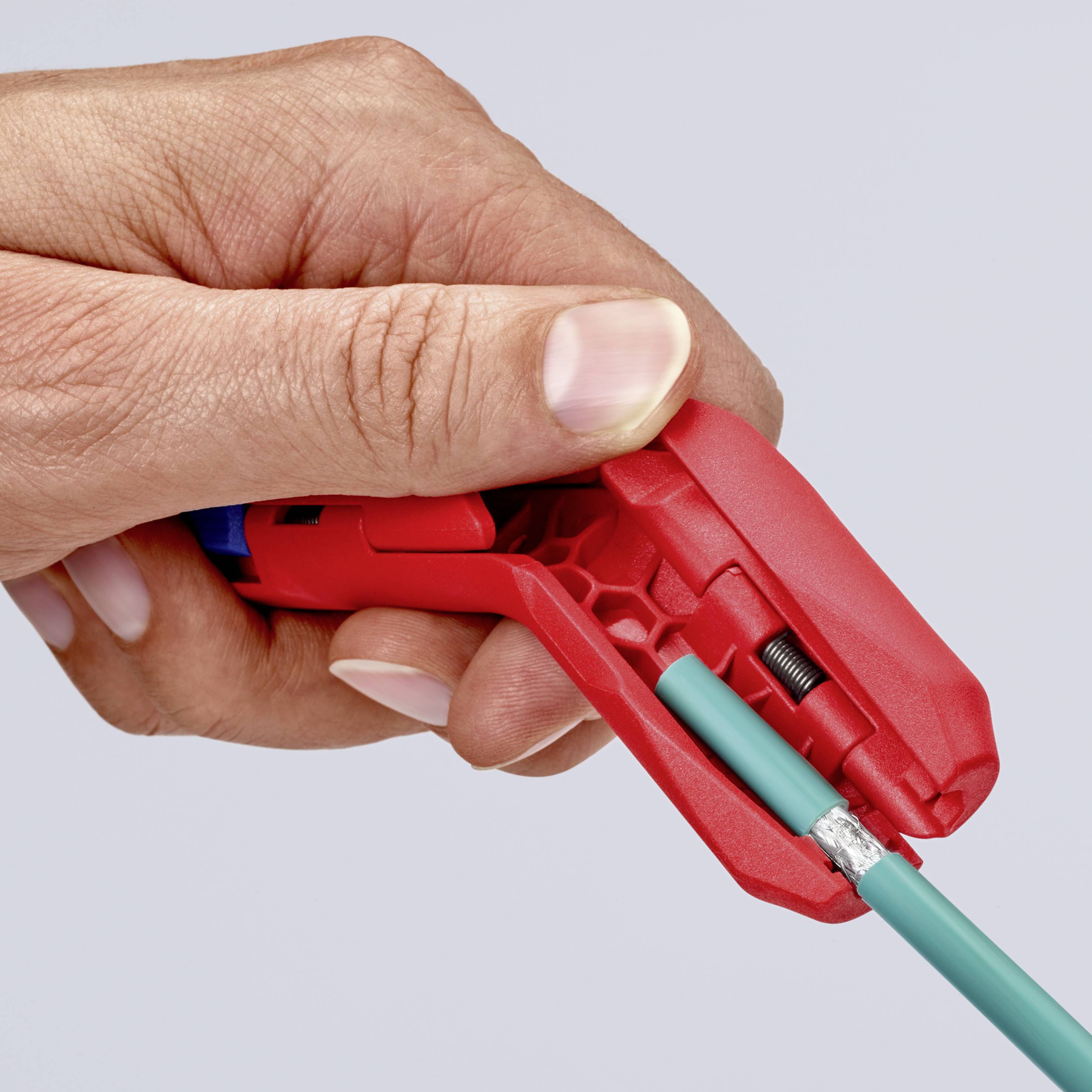 Eine Hand hält einen roten Abisolierer, der einen grünen Draht streift. Der Draht wird präzise bearbeitet, um die Isolierung zu entfernen.