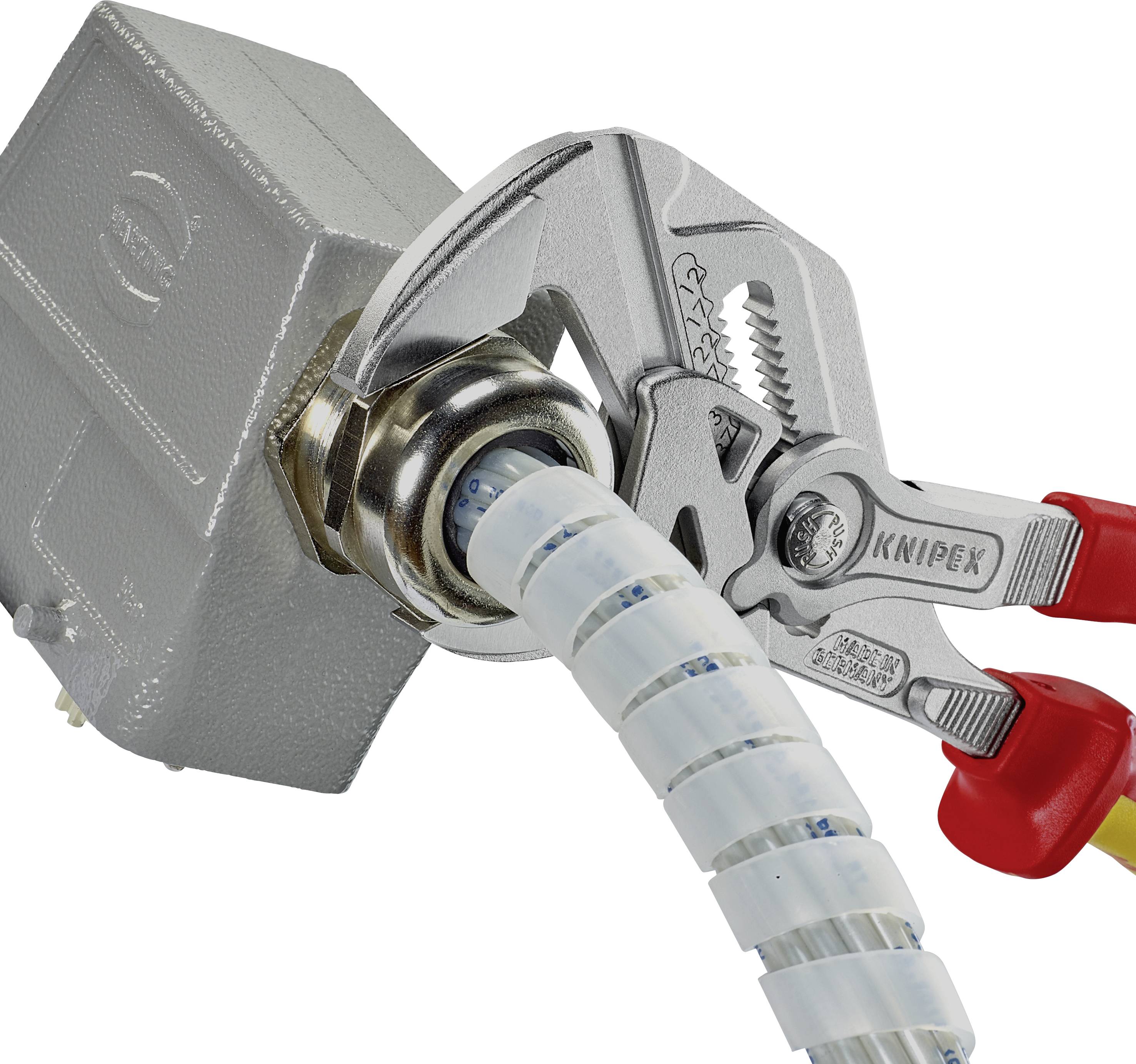 Eine Zange greift eine Metallmutter an einem Kabel, das aus einer Anschlussdose führt. Die Zange hat rote Griffe.