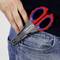 Eine Hand steckt eine rote und blaue Schere mit der Aufschrift 'Knipex' in die Gesäßtasche einer blauen Jeans.