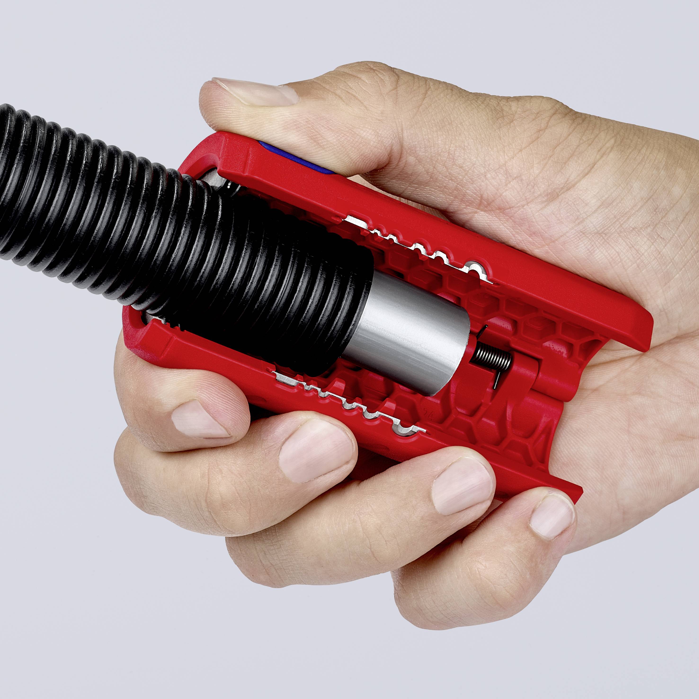 Hand hält eine rote Kabelschere, die ein schwarzes Kabel anschneidet.