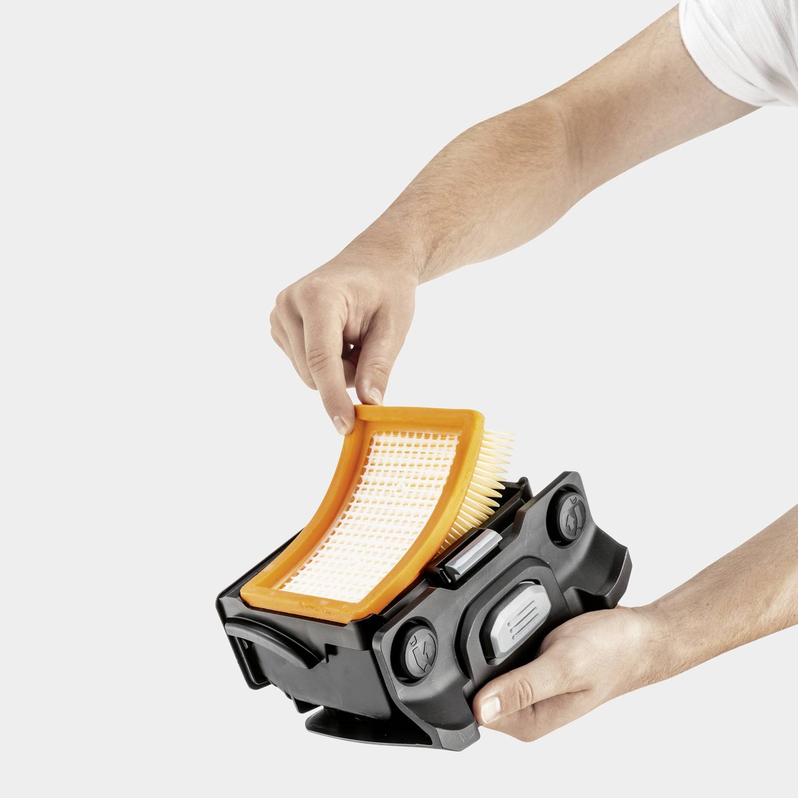 Eine Person schiebt einen orangefarbenen Filter in ein schwarzes Gerät, möglicherweise einen Staubsauger oder Luftreiniger.