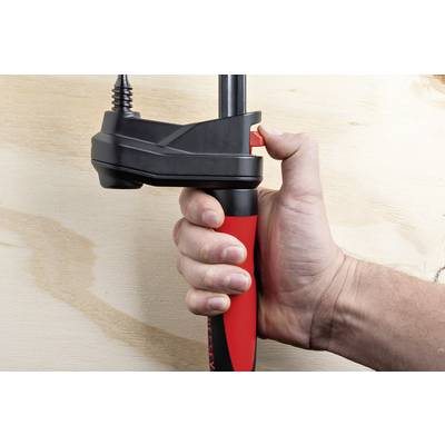 Eine Hand hält eine Zwinge, die an einem Holzbrett befestigt ist. Die Person drückt den Hebel, um die Klemme zu lösen oder festzuziehen.