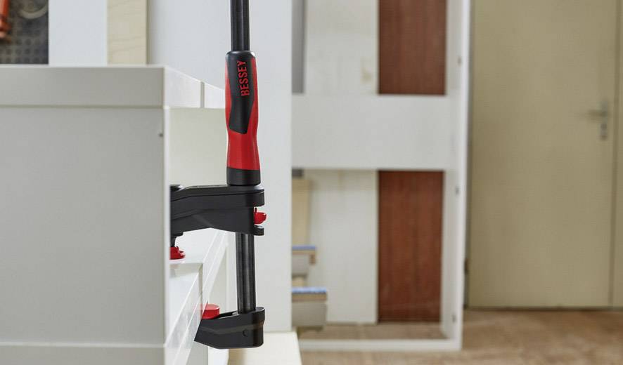 Ein Schrank wird mit einer Klemme von der Marke Bessey fixiert. Im Hintergrund sind Holz und eine Tür zu sehen.