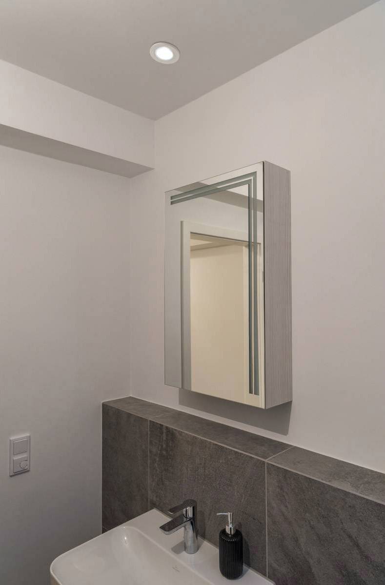 Kleines Badezimmer mit Waschbecken, Spiegel und dunklen Fliesen. Minimalistisches Design in neutralen Farben.