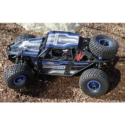 Ein RC-Buggy mit der Aufschrift 'Raptor 6S' und 'Arrma' in blau und schwarz, steht auf Erde. Das Auto hat große, grob profilierte Reifen.