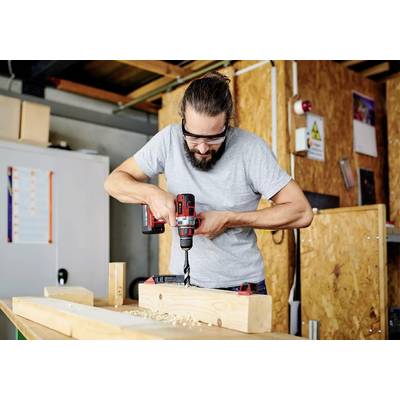 Mann mit Schutzbrille, der in einer Werkstattumgebung eine Bohrmaschine verwendet, um Löcher in Holzbretter zu bohren.