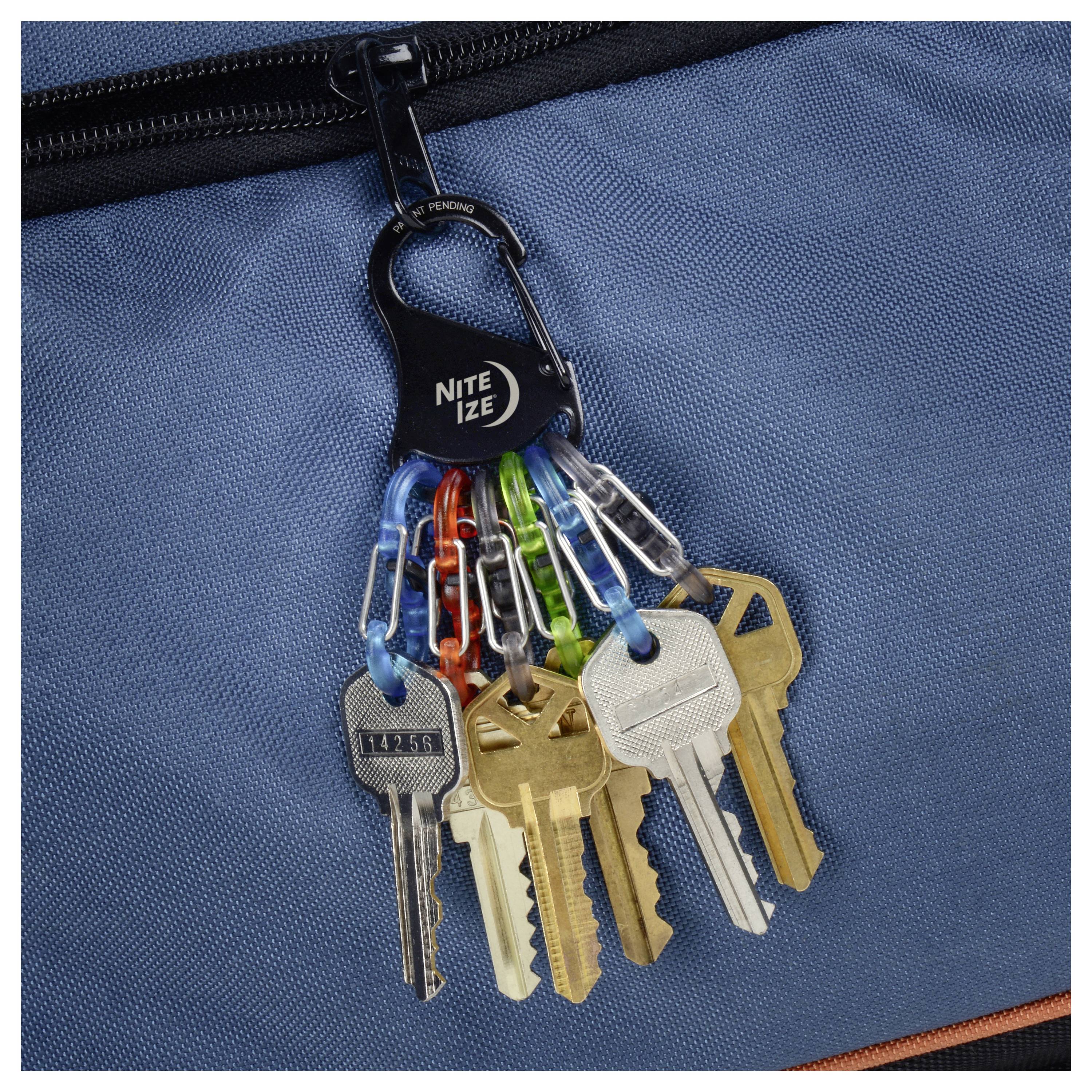 Ein Schlüsselbund an einer blauen Tasche, befestigt mit einem schwarzen Karabiner mit der Aufschrift "Nite Ize", der Schlüssel in verschiedenen Farben und Formen umfasst.