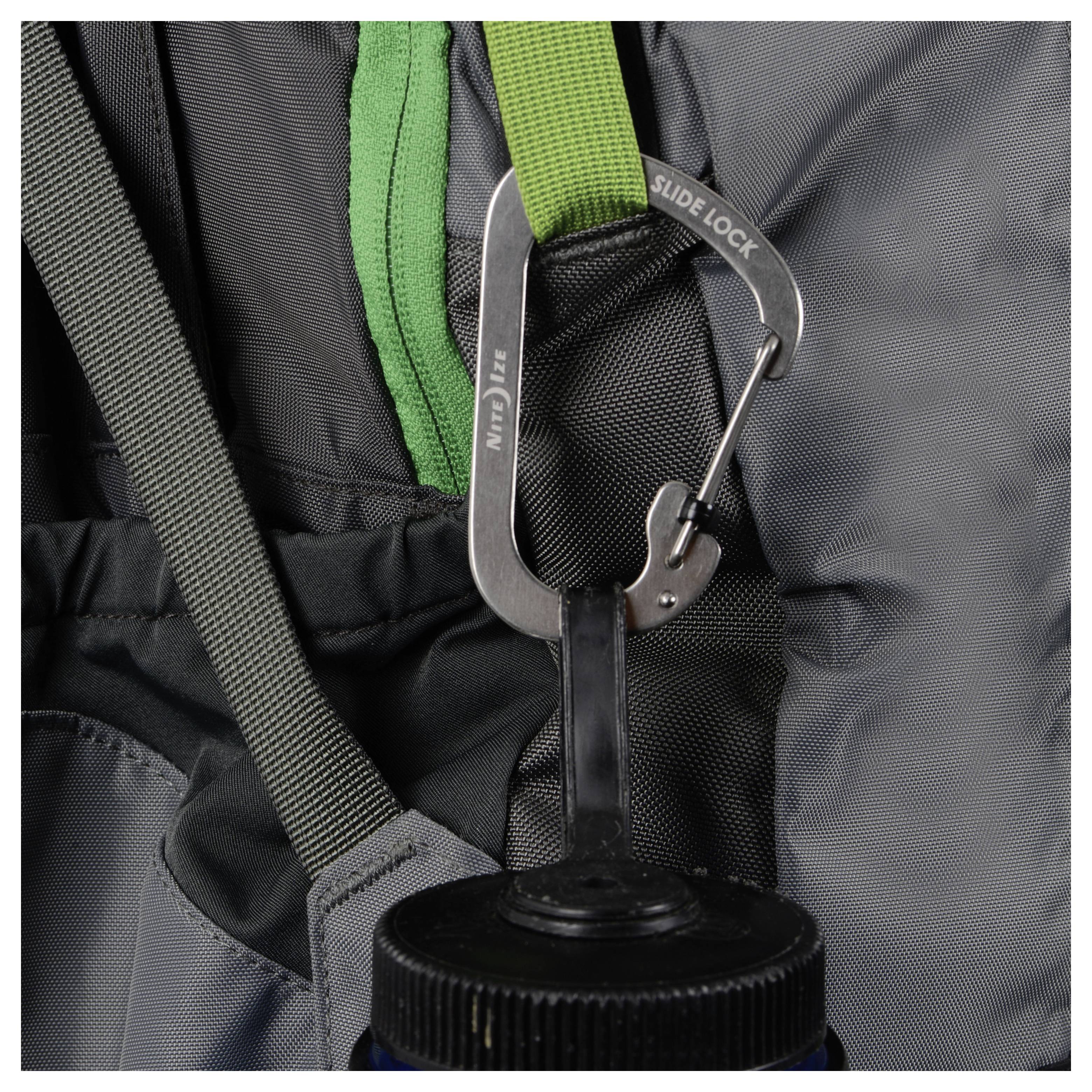 Ein Karabiner mit der Beschriftung "Slide Lock" sichert eine Wasserflasche an einem grauen Rucksack. Die Flasche hängt an einer schwarzen Schlaufe, die am Karabiner befestigt ist.