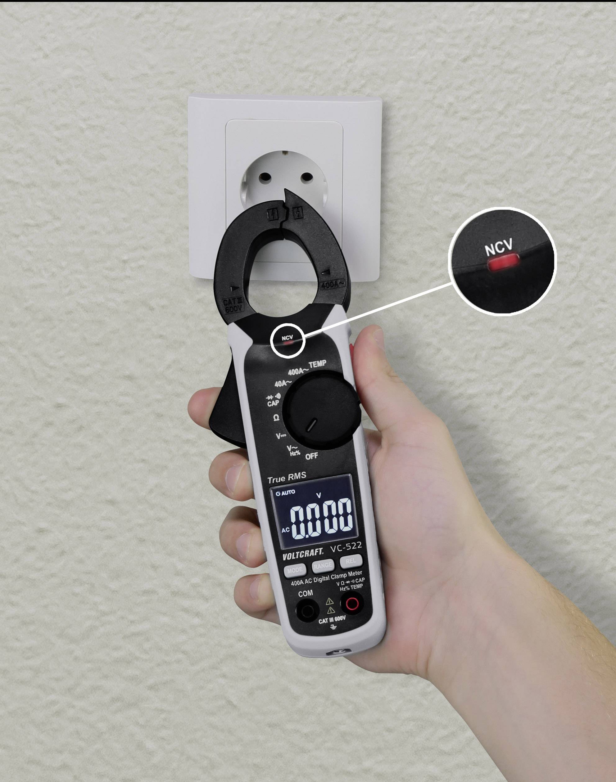 'Multimeter wird an Steckdose gehalten, zeigt 0,00 Volt. Nahansicht des NCV-Knopfes. Wandsteckdose im Hintergrund.'