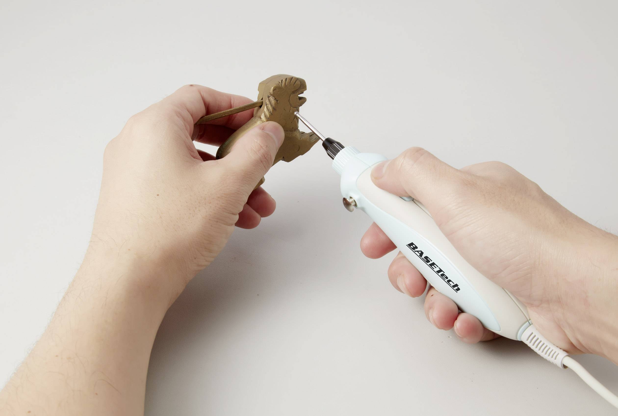 Zwei Hände halten einen kleinen Holzblock, der mit einem elektrischen Werkzeug geschnitzt wird.