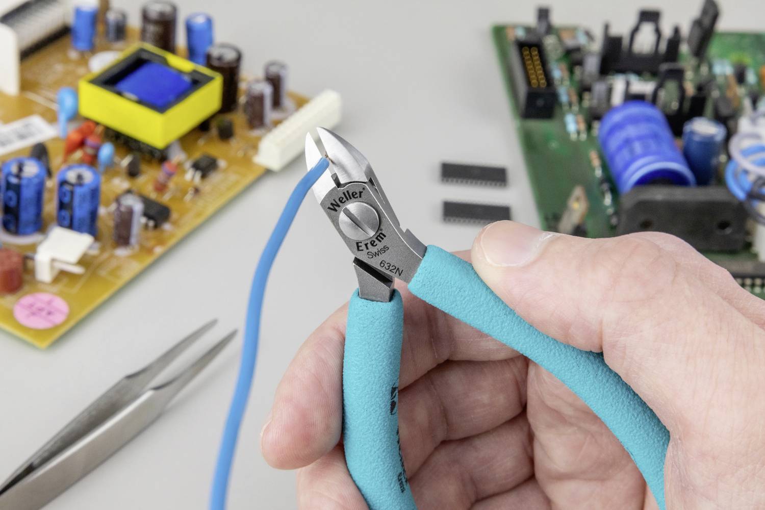 Eine Hand hält einen Seitenschneider nahe einer Leiterplatte mit verschiedenen elektronischen Bauteilen.