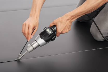 Eine Person verwendet ein Heißluft-Schweißgerät, um eine Naht auf schwarzem Material zu verschweißen. Professionelles Handwerk.