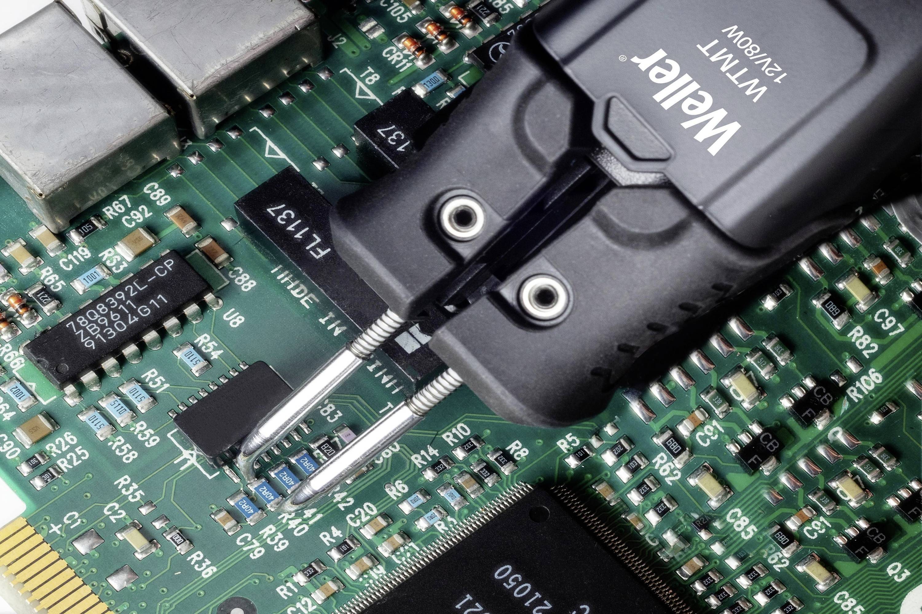 Lötstation mit zwei Spitzen bearbeitet eine grüne Leiterplatte mit mehreren elektronischen Komponenten und Chips.