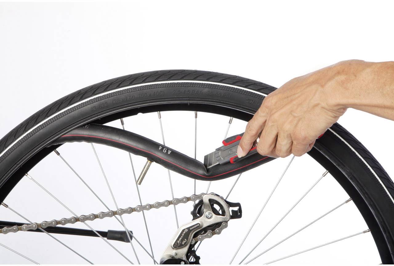 Eine Hand benutzt ein Werkzeug, um einen Fahrradreifen an einer Felge zu montieren. Das Bild zeigt den Mechanismus des Einbaus.