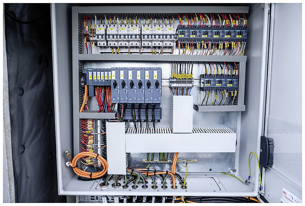 Elektrischer Schaltschrank mit offenen Türen, zeigt Verdrahtungen, Sicherungen und Schalter. Komponenten sind farblich markiert.