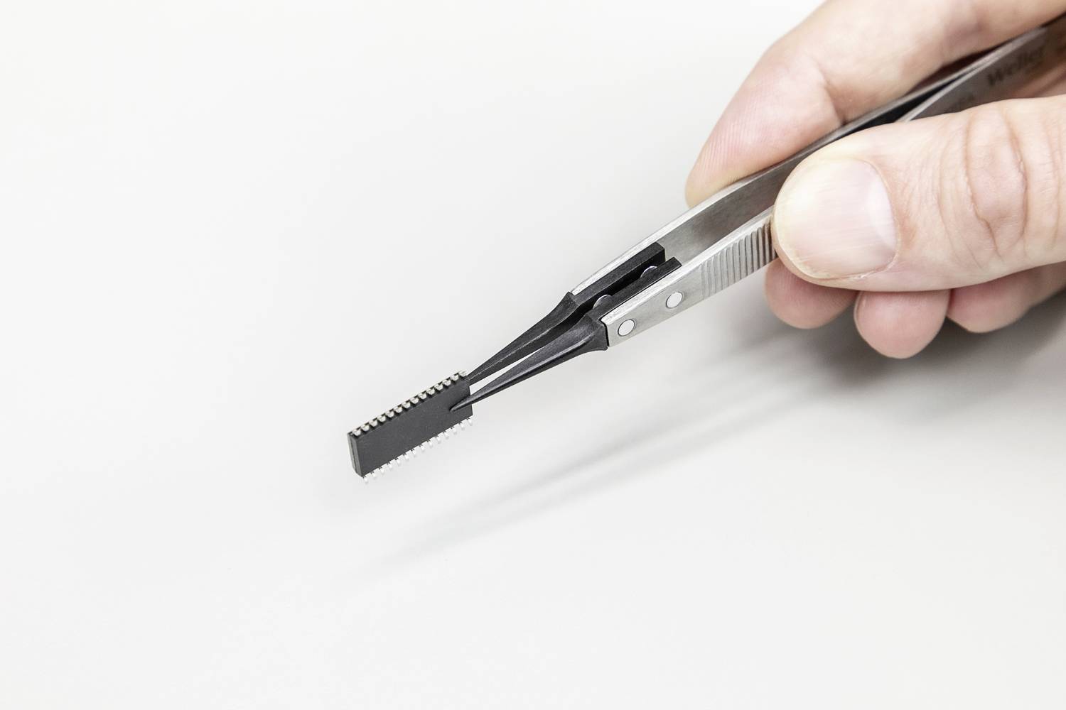Eine Hand hält eine Präzisionspinzette mit einem geriffelten Ende, das für feine Arbeiten geeignet ist.