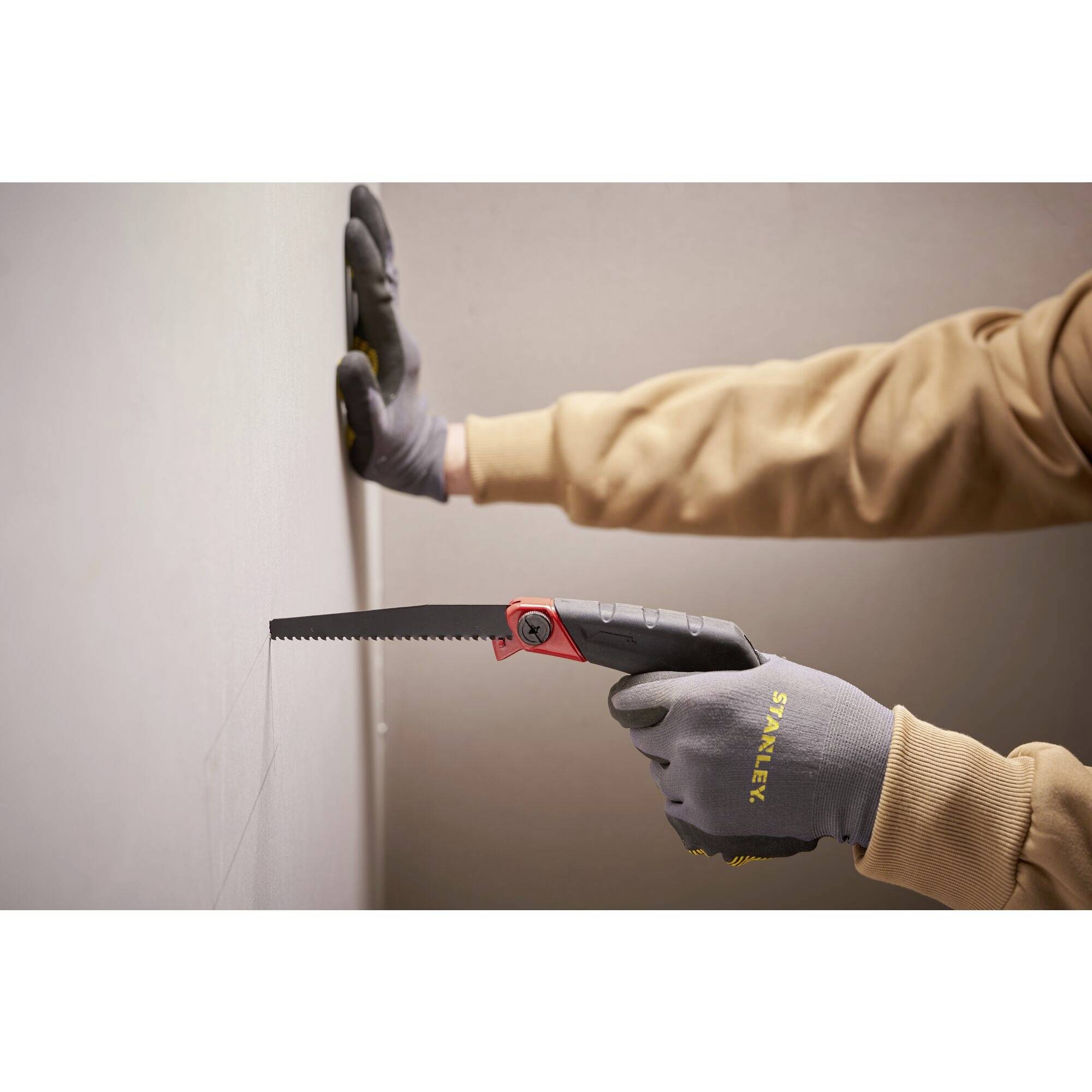 Person mit Handschuhen, die eine Handsäge hält und eine Wand sägt, Innenraumarbeitsszene.