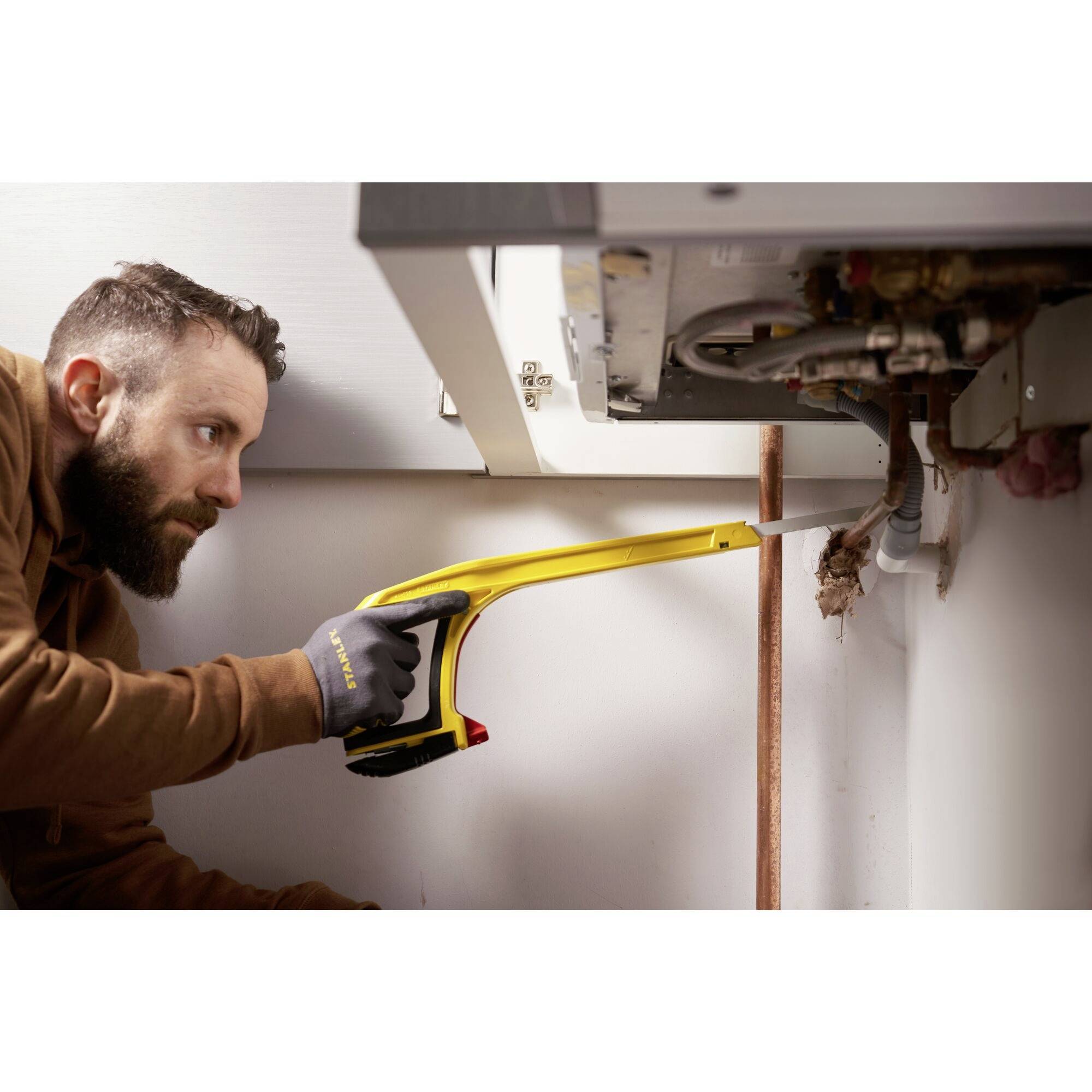 Ein Mann benutzt ein Inspektionswerkzeug, um die Rohrleitungen eines Heizkessels zu überprüfen. Er trägt einen braunen Pullover und Handschuhe.