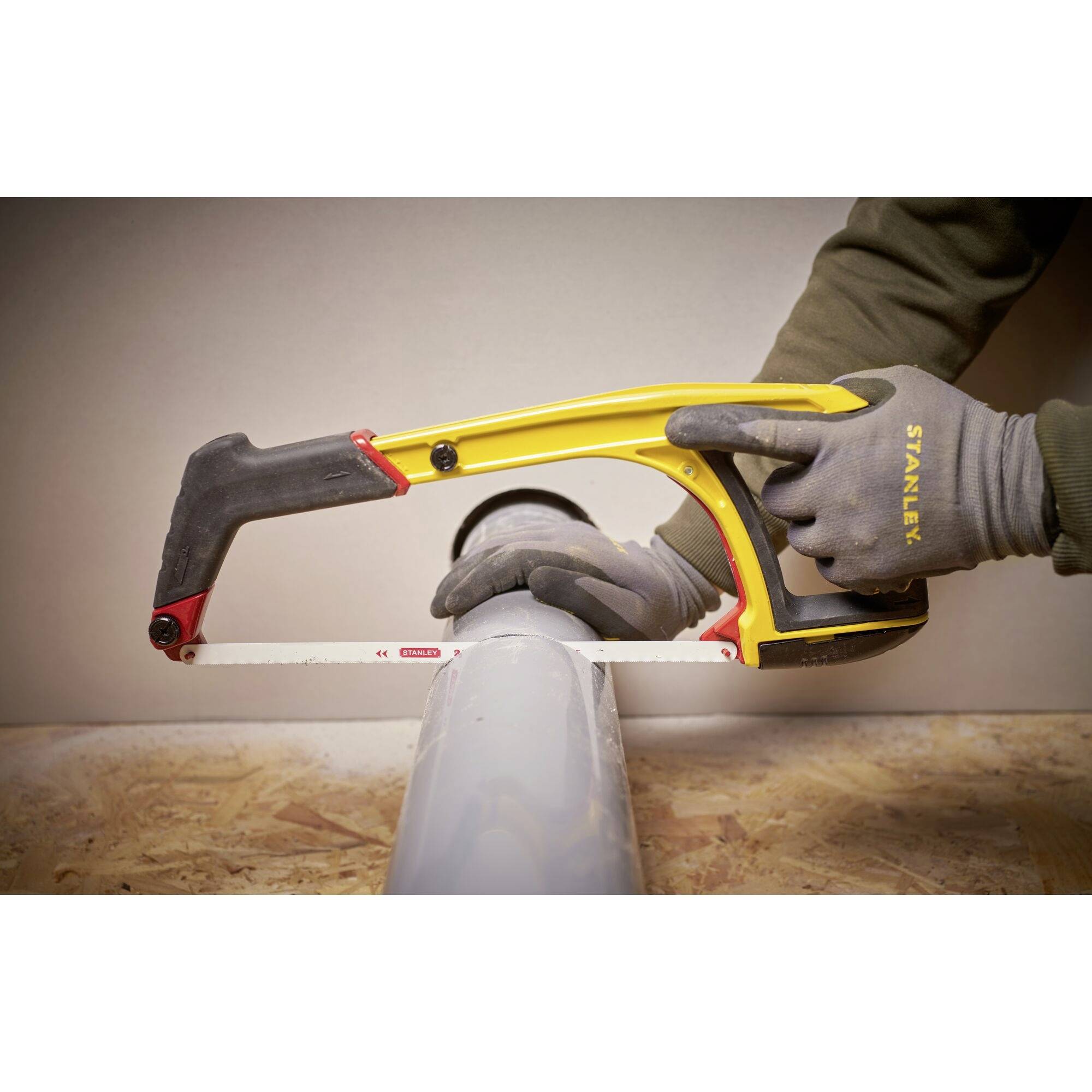 Eine Person sägt mit einer Handsäge ein Kunststoffrohr. Die Säge hat einen gelben Griff. Es werden Arbeitshandschuhe getragen.