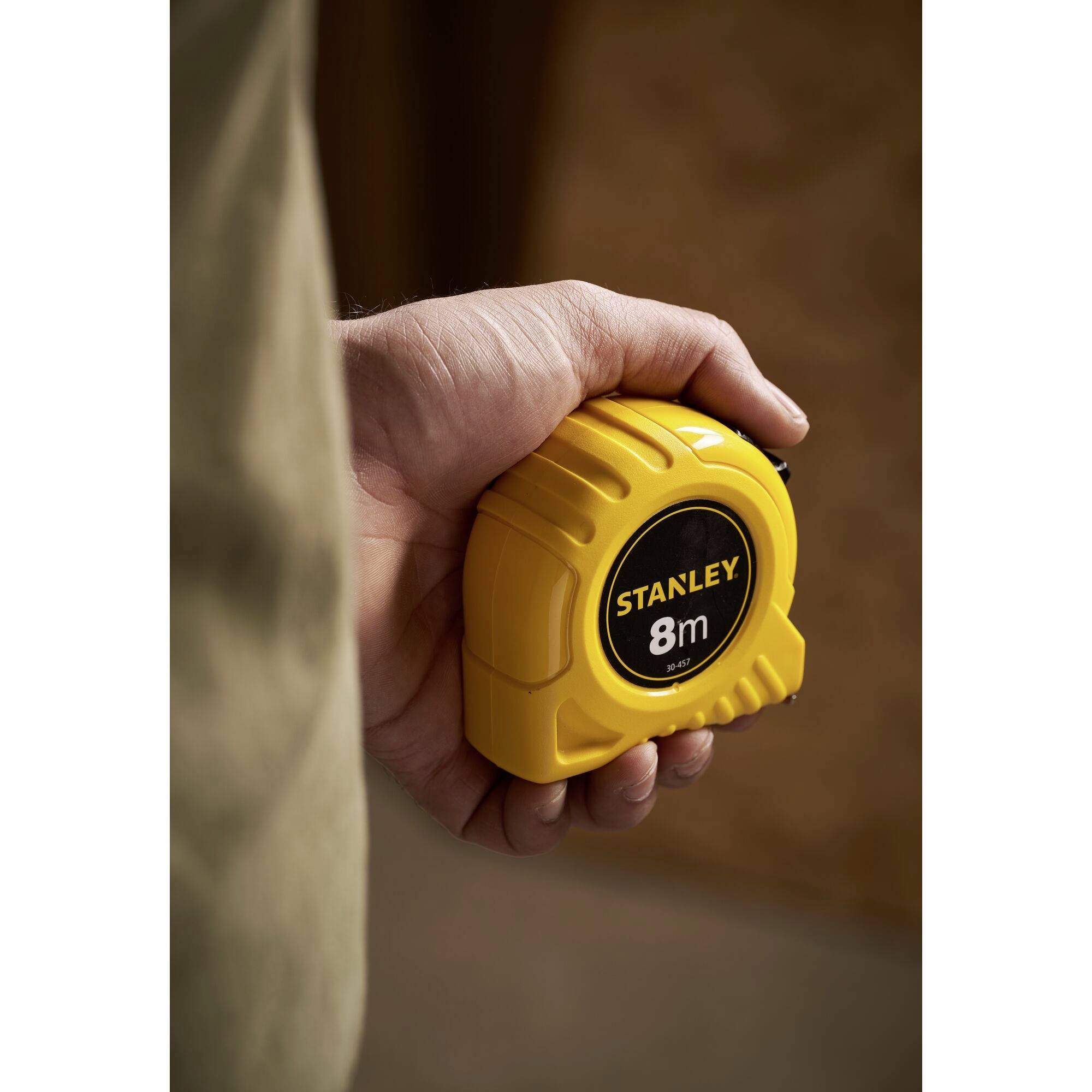 Eine Hand hält ein gelbes Maßband mit der Aufschrift 'STANLEY 8m'.