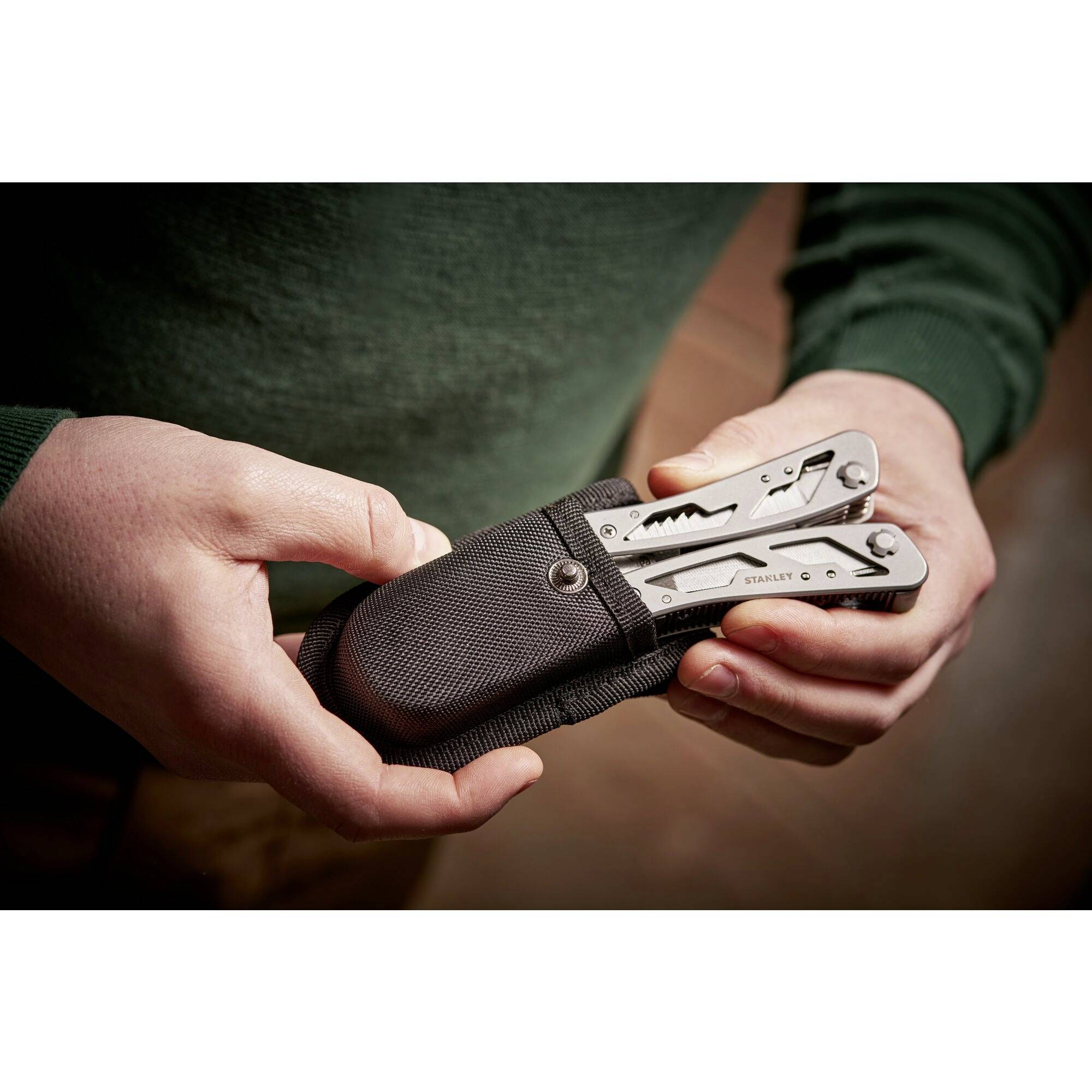 Person hält ein Multitool aus Metall in einem schwarzen Etui in der Hand. Das Multitool ist teilweise geöffnet und zeigt seine Funktionen.