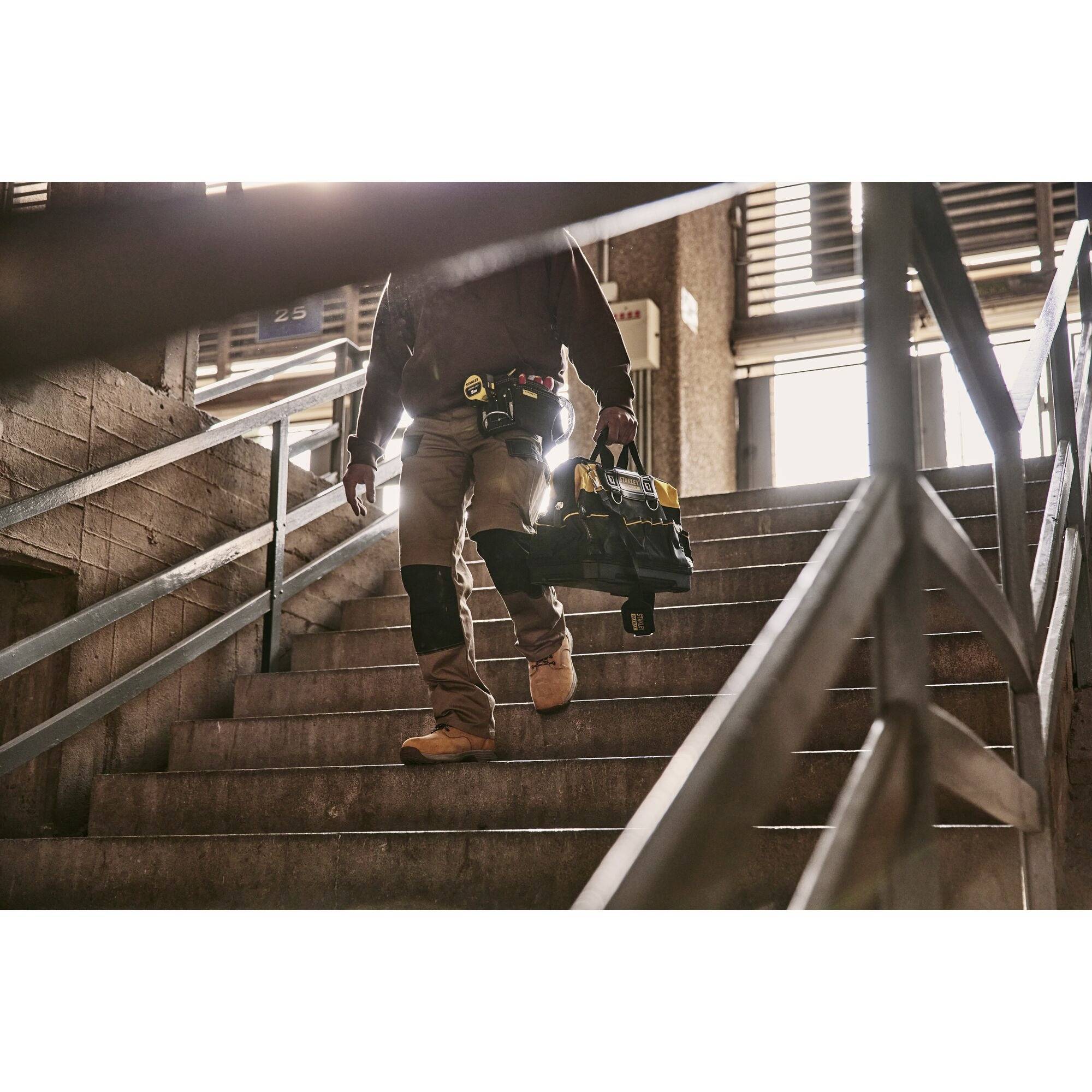 Ein Bauarbeiter geht eine Treppe hinauf, trägt eine Werkzeugtasche und trägt Stiefel und Schutzkleidung.