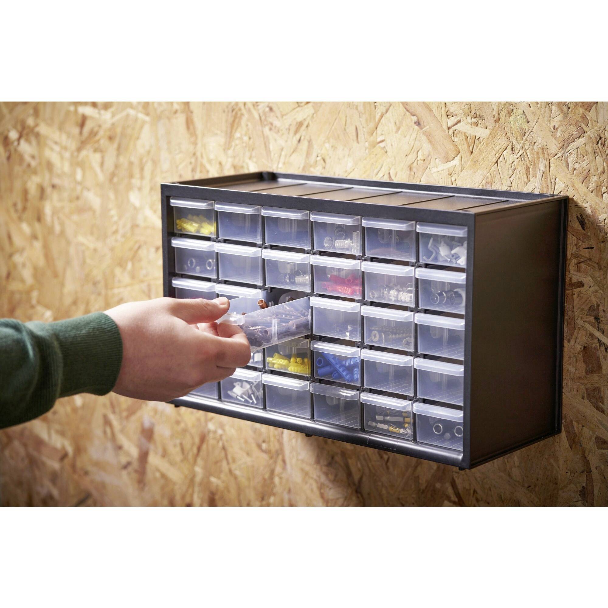 Ein Regal mit vielen kleinen Schubladen, gefüllt mit verschiedenen Werkzeugteilen, wird von einer Hand geöffnet. Schubladensystem zur Werkzeugaufbewahrung.