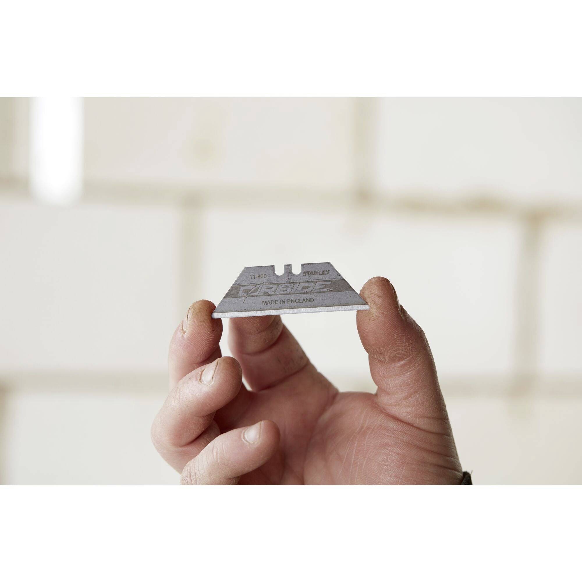 'Nahaufnahme einer Hand, die eine scharfe Rasierklinge hält, auf der "Made in England" steht, mit verschwommenem Hintergrund.'