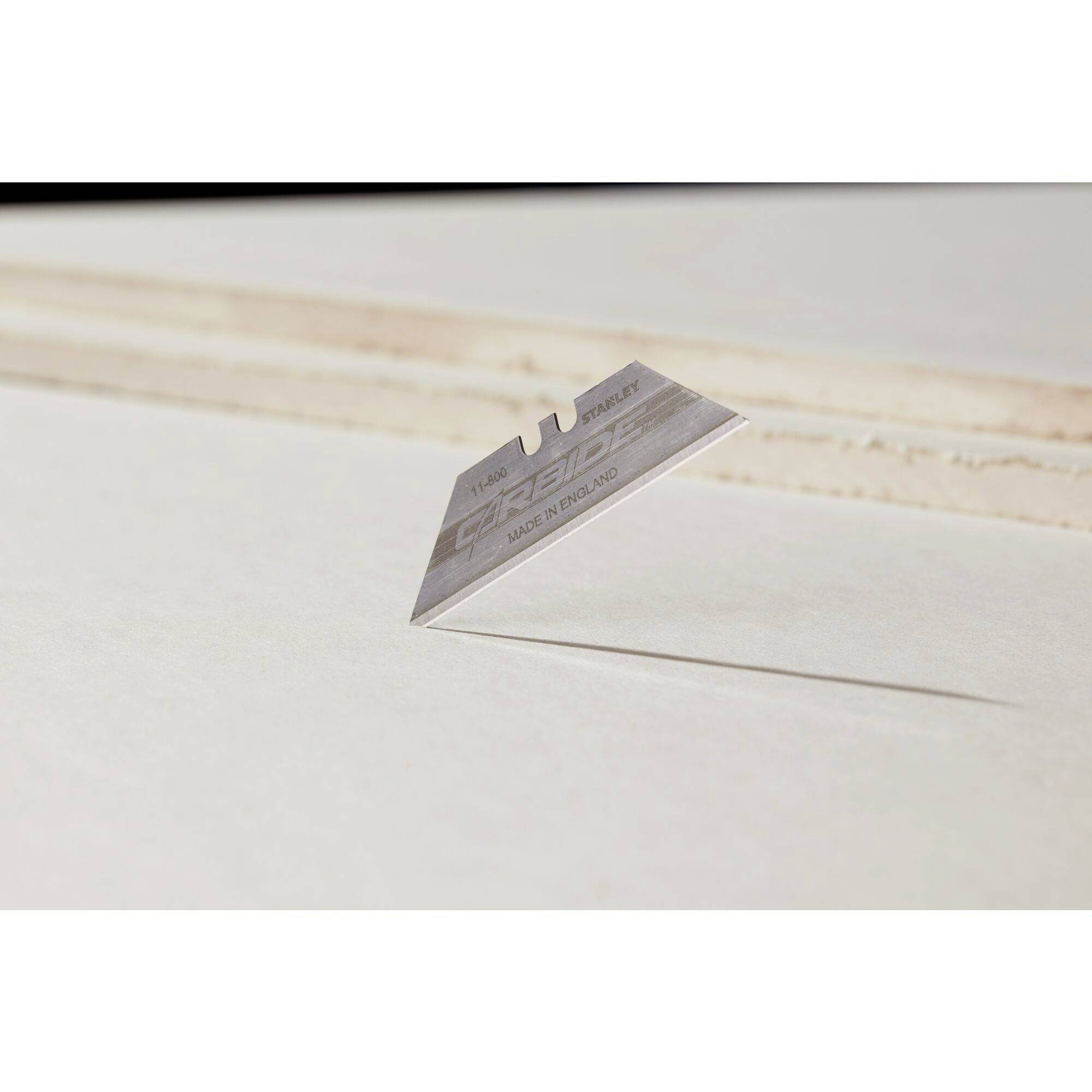 Eine einzelne Rasierklinge schwebt über einer Oberfläche, wirft einen deutlichen Schatten. Hintergrund ist unscharf und hell.