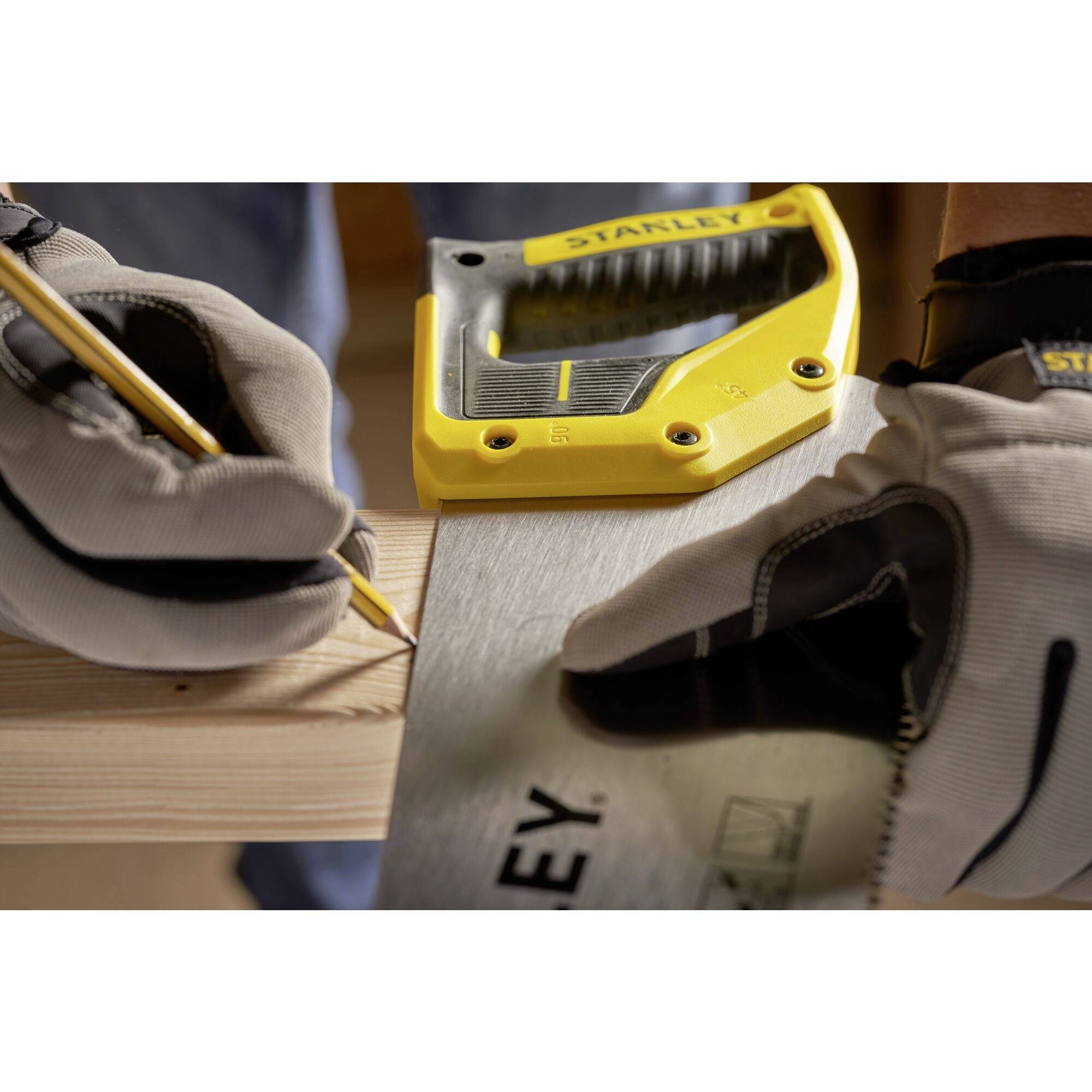 Eine Person mit Handschuhen markiert mit einem Bleistift ein Stück Holz mit einem gelben Maßwerkzeug und sägt es ab.
