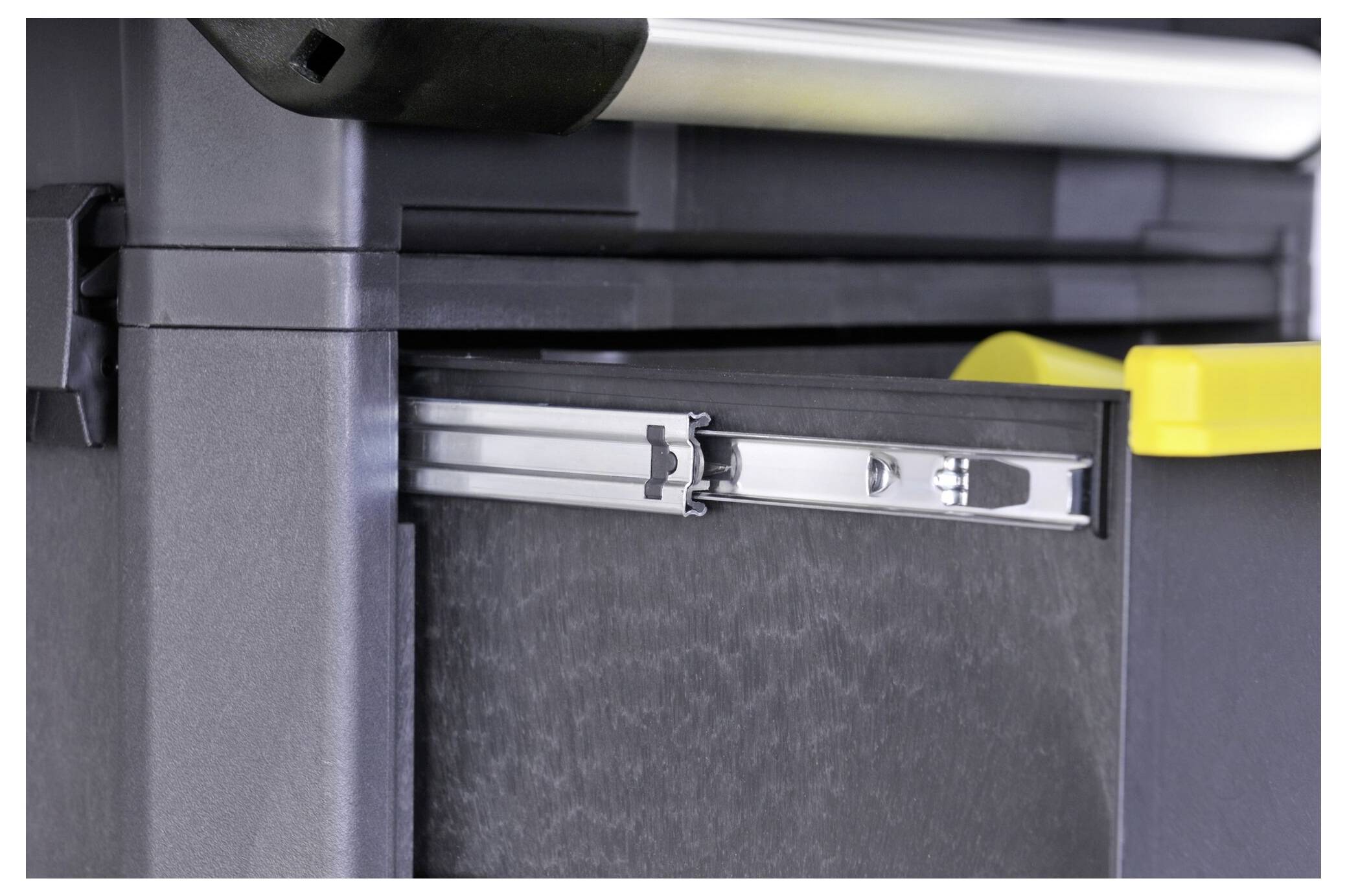 Graue Schubladenführung in einem schwarzen Schrank, teilweise geöffnet, mit gelbem Verschlussmechanismus.
