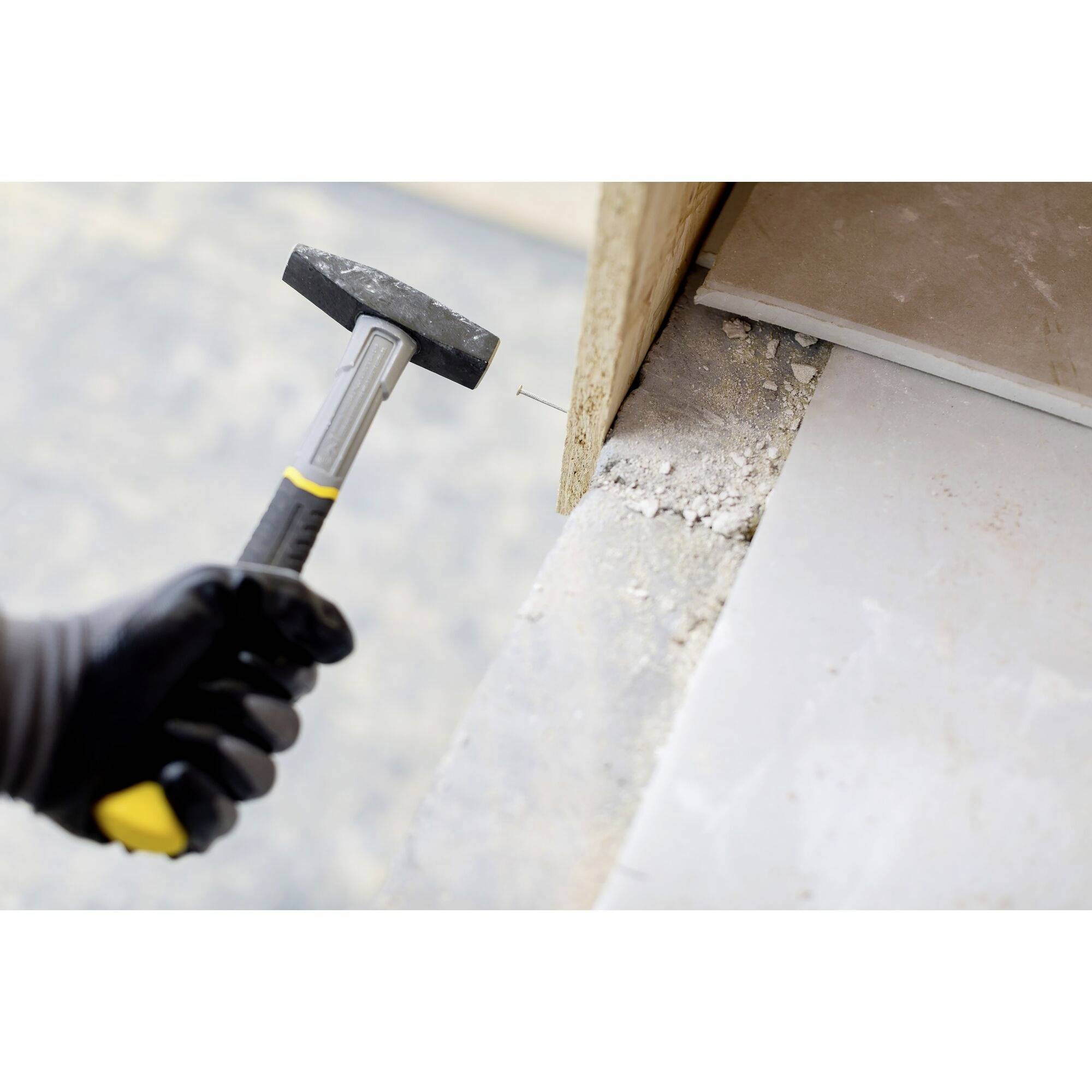 Eine Person mit Handschuh hält einen Hammer und zieht einen Nagel aus einem Holzbrettrand auf einer Baustelle heraus.