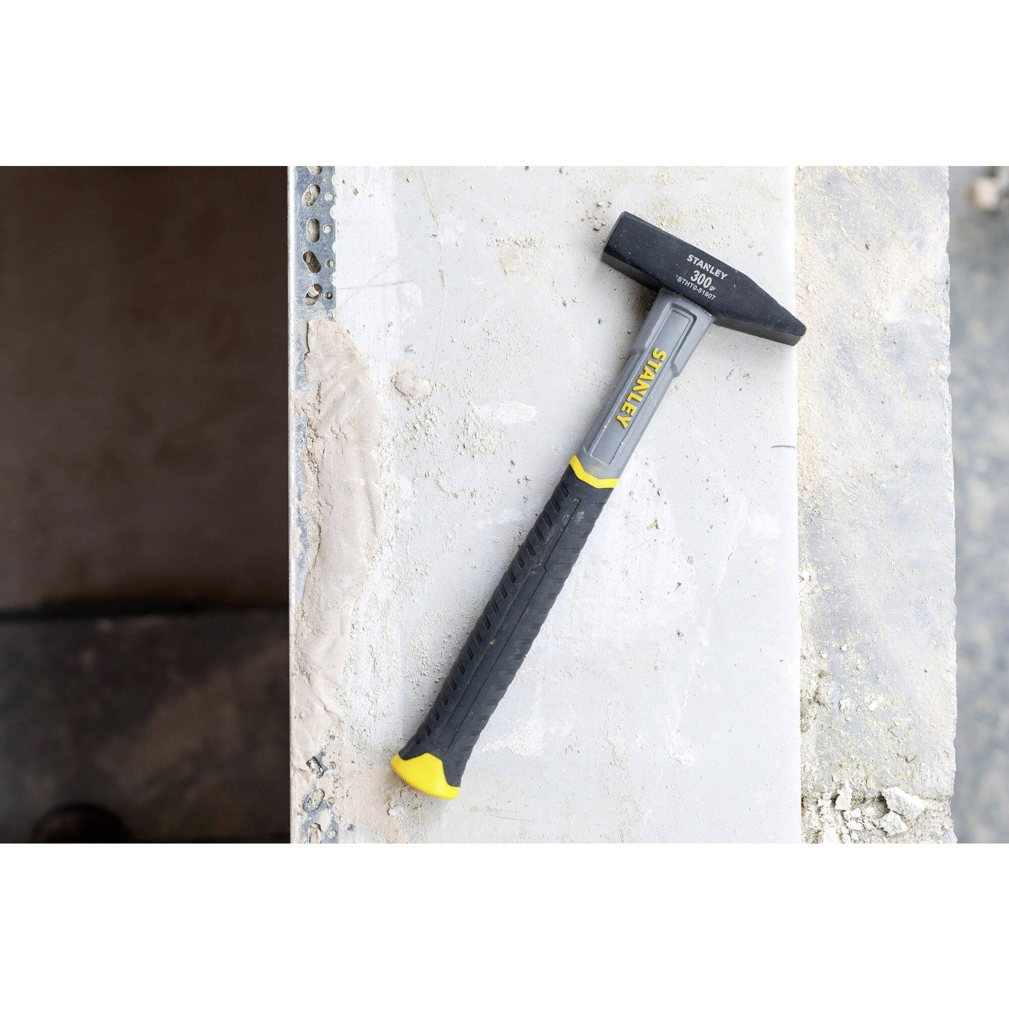 Ein Hammer liegt auf einer Betonfläche. Der Griff ist schwarz und gelb; rechts unten befindet sich eine raue Oberfläche.