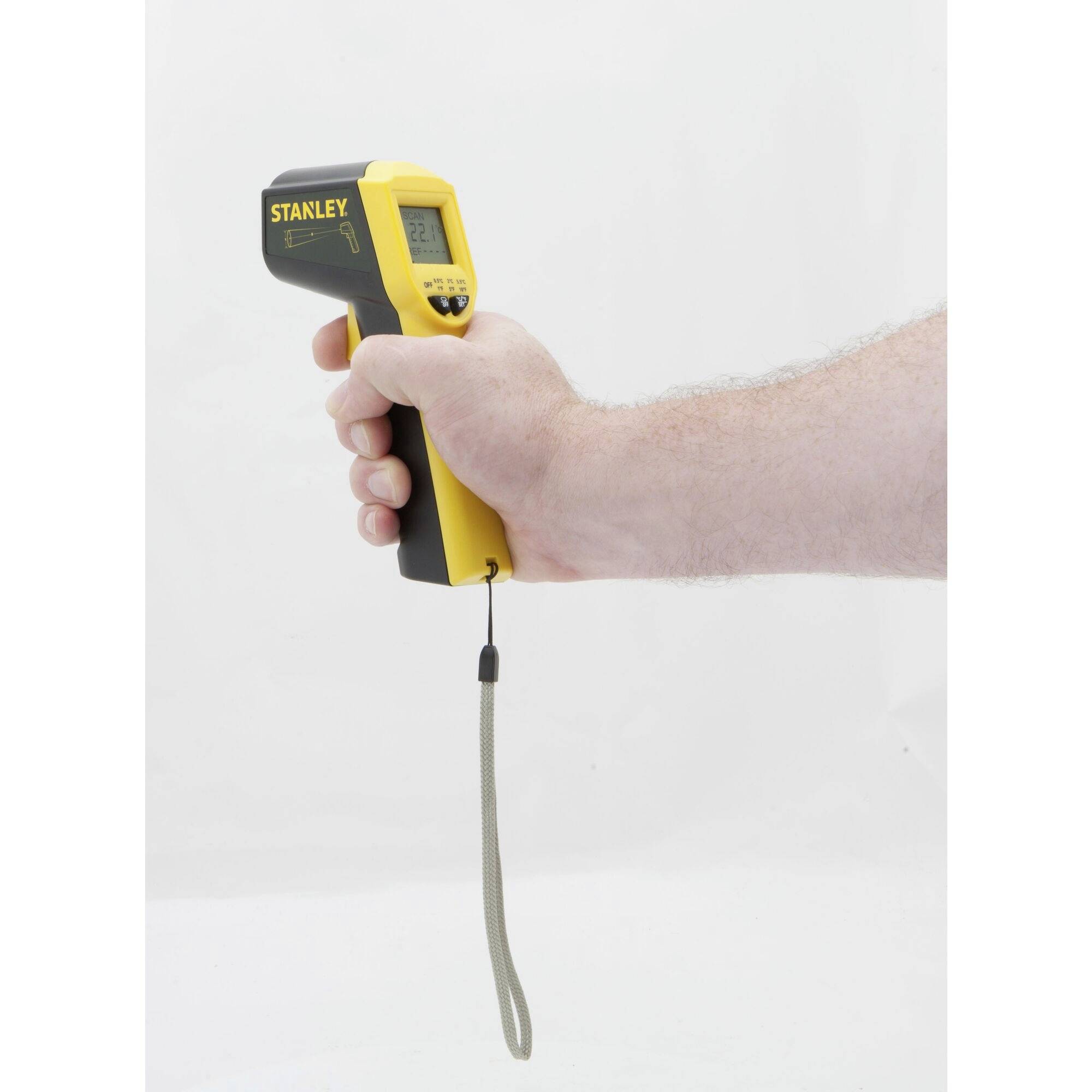 Eine Person hält ein gelbes Infrarot-Thermometer mit Anzeige in der Hand, zeigt es auf eine weiße Fläche.