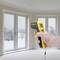 Hand hält ein Infrarot-Thermometer in einem Raum mit schneebedeckter Landschaft durch Fenster. Temperaturmessung wird durchgeführt.
