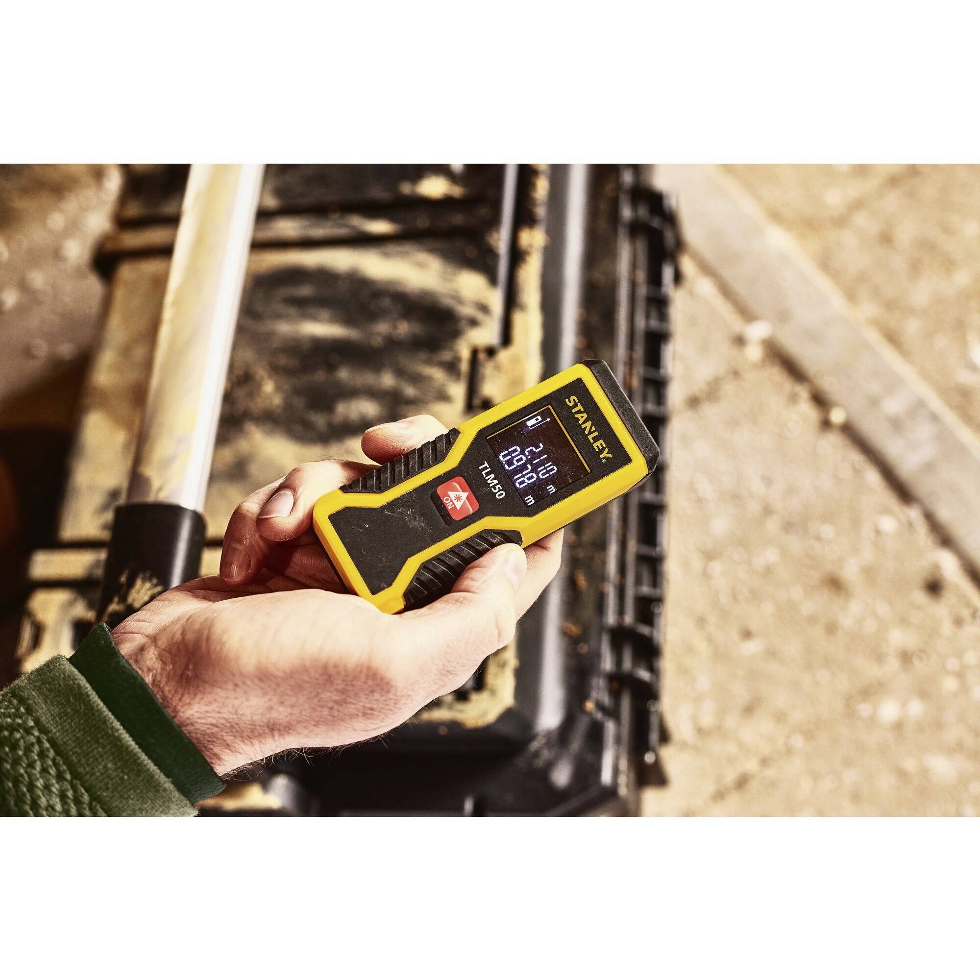 Eine Hand hält ein digitales gelbes Messgerät, das 0,12 Meter anzeigt. Im Hintergrund ist ein Werkzeugkasten zu sehen.