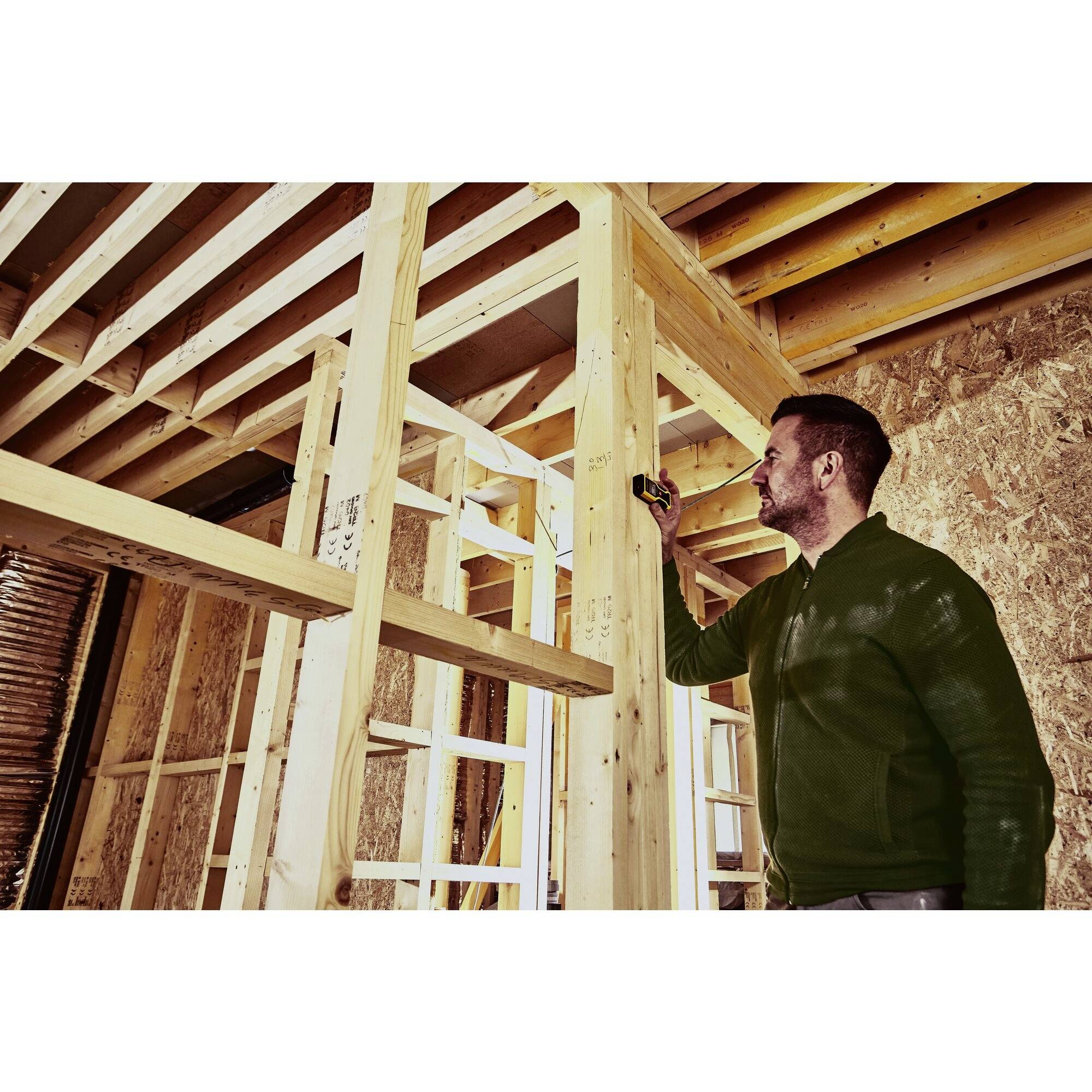 Eine Person vermisst mit einem Maßband einen Holzrahmen in einem im Bau befindlichen Raum.